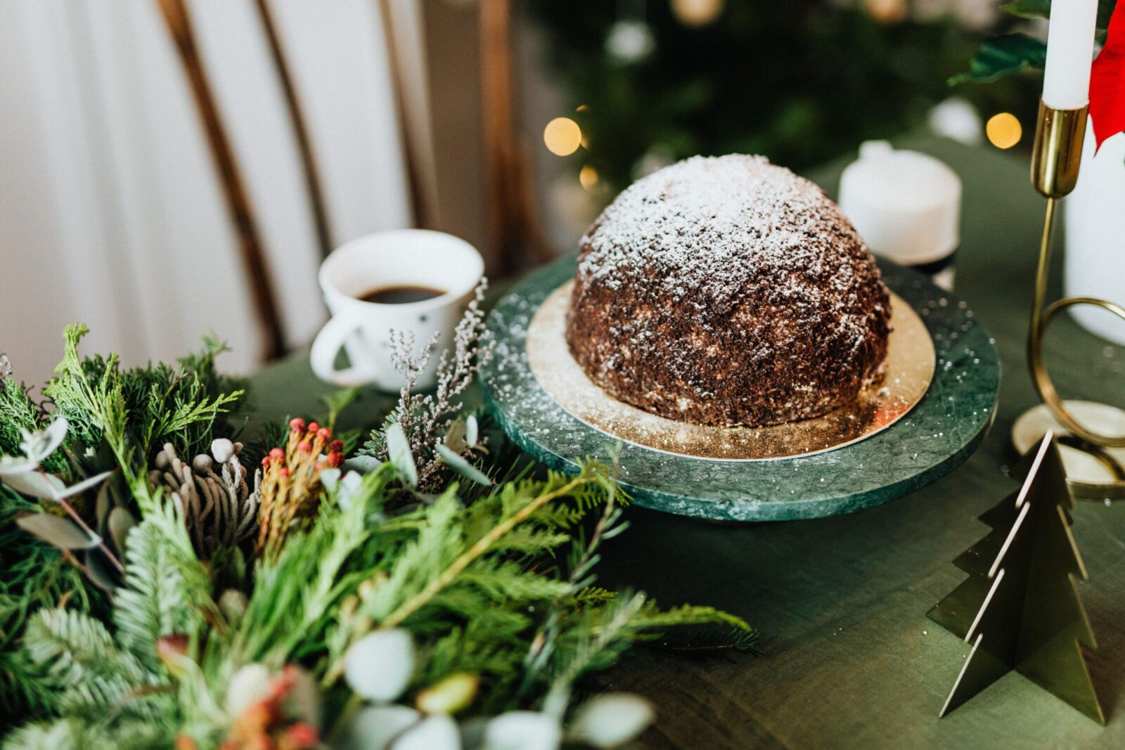 Festive Christmas pudding with coffee served on a green table, adorned with seasonal decorations.